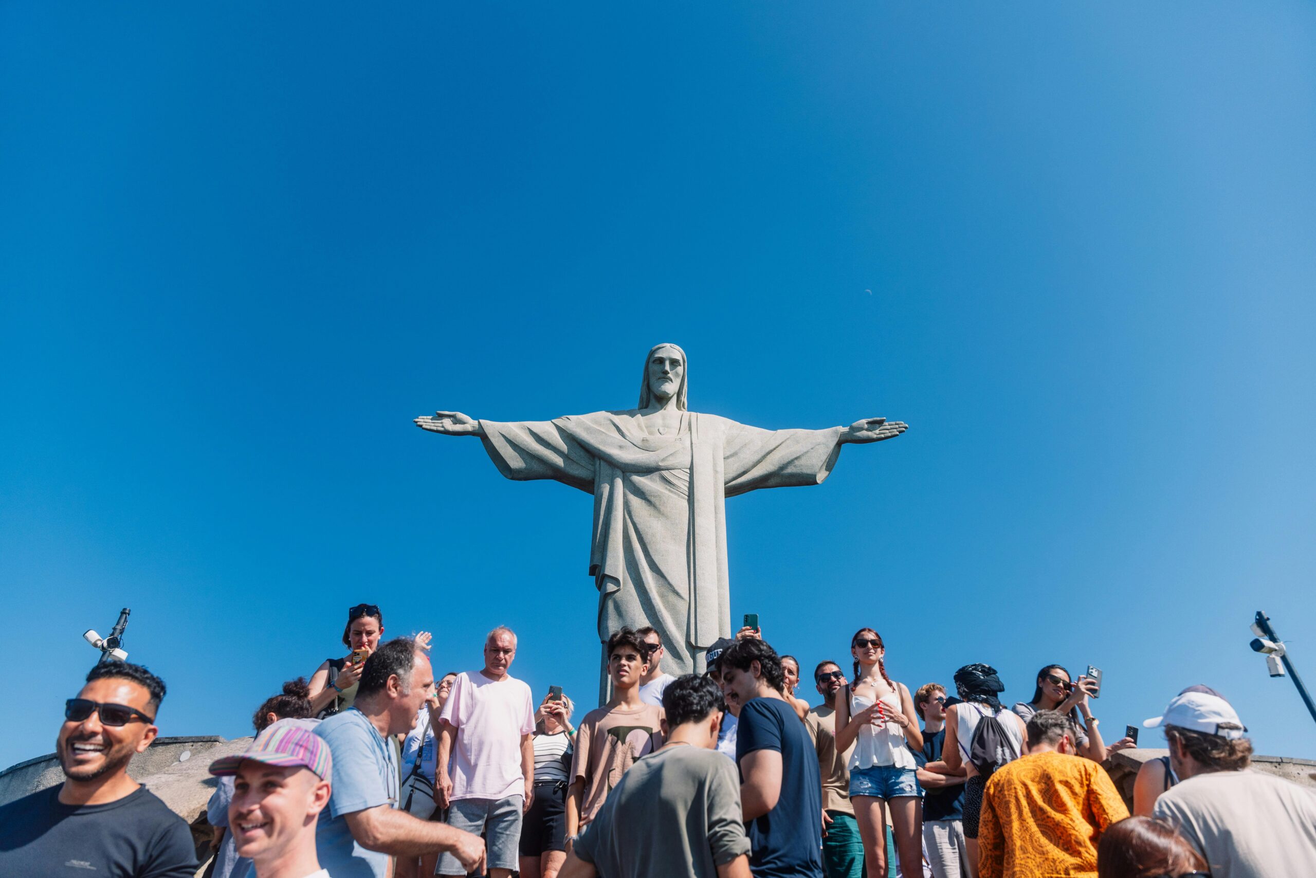 Tourists gather at the iconic Christ the Redeemer statue under clear blue skies in Rio de Janeiro, Brazil.
