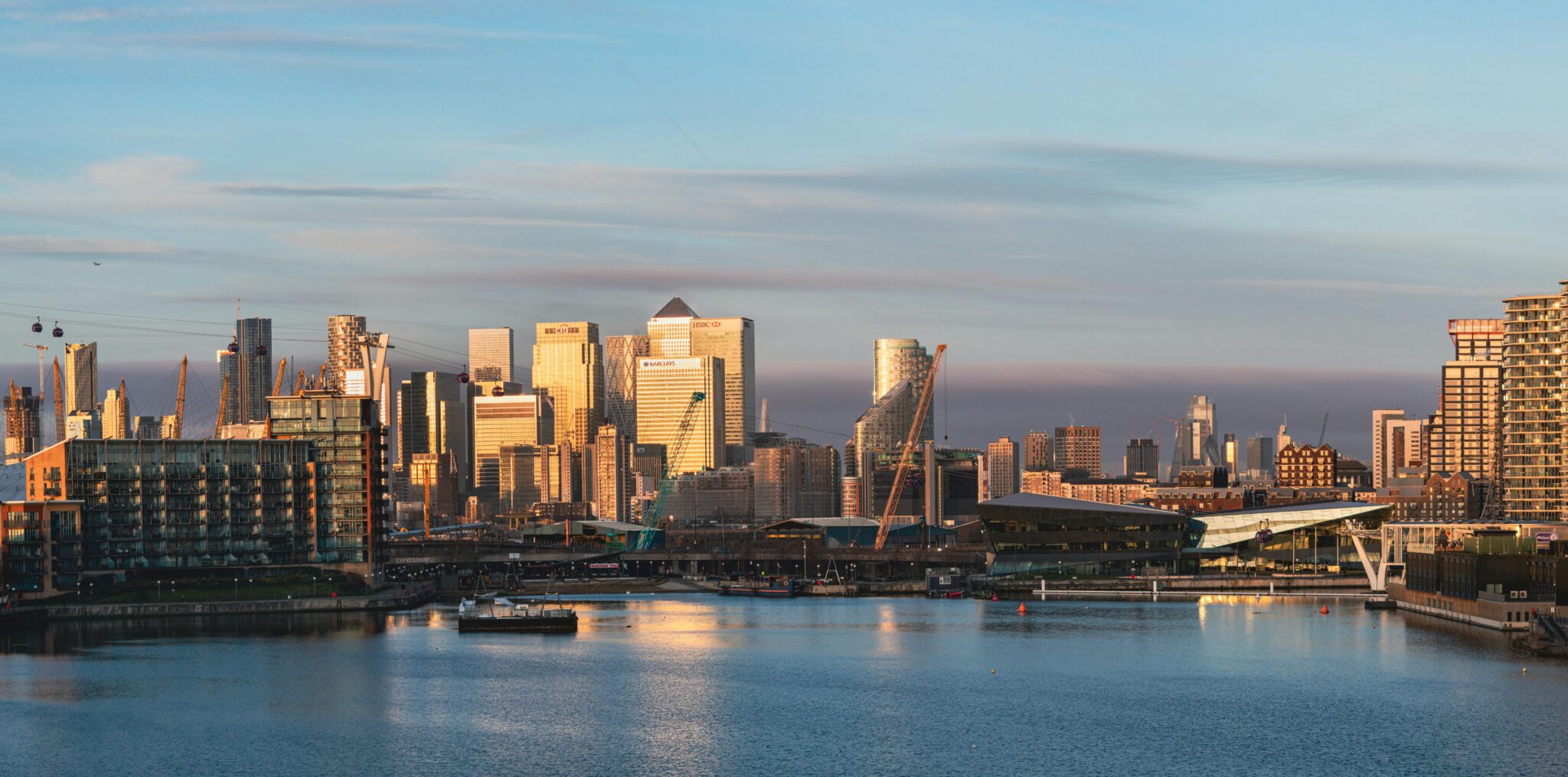 Home Captivating sunrise view of London's Royal Docks with towering skyscrapers reflecting in calm waters.