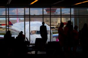 Silhouettes of travelers waiting at an airport terminal with an airplane visible through the window.
