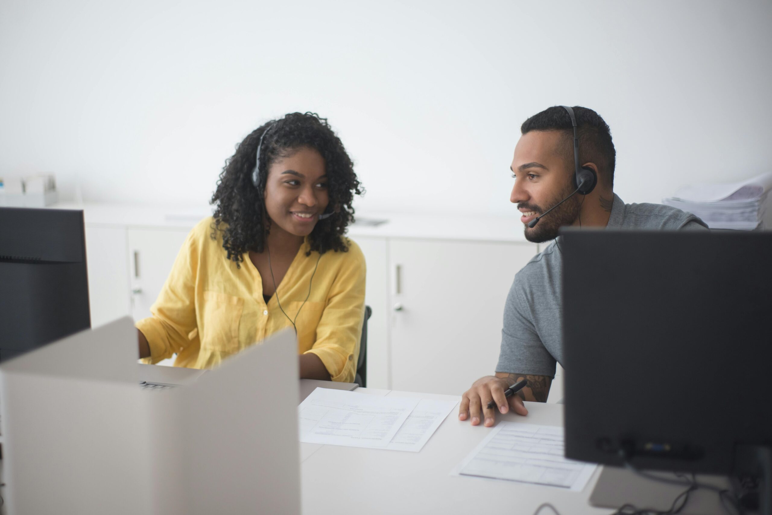 Two call center agents working together with headsets in a modern office environment.